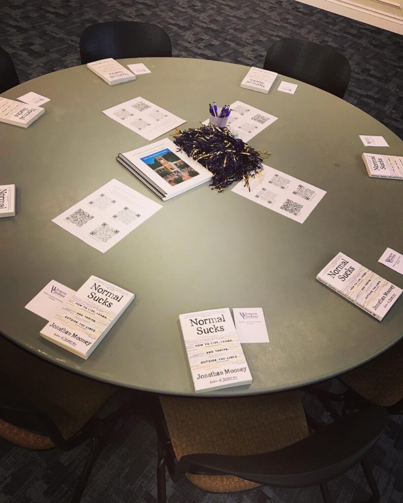 Image of table top with seven table settings with books, notepaper and decorations.